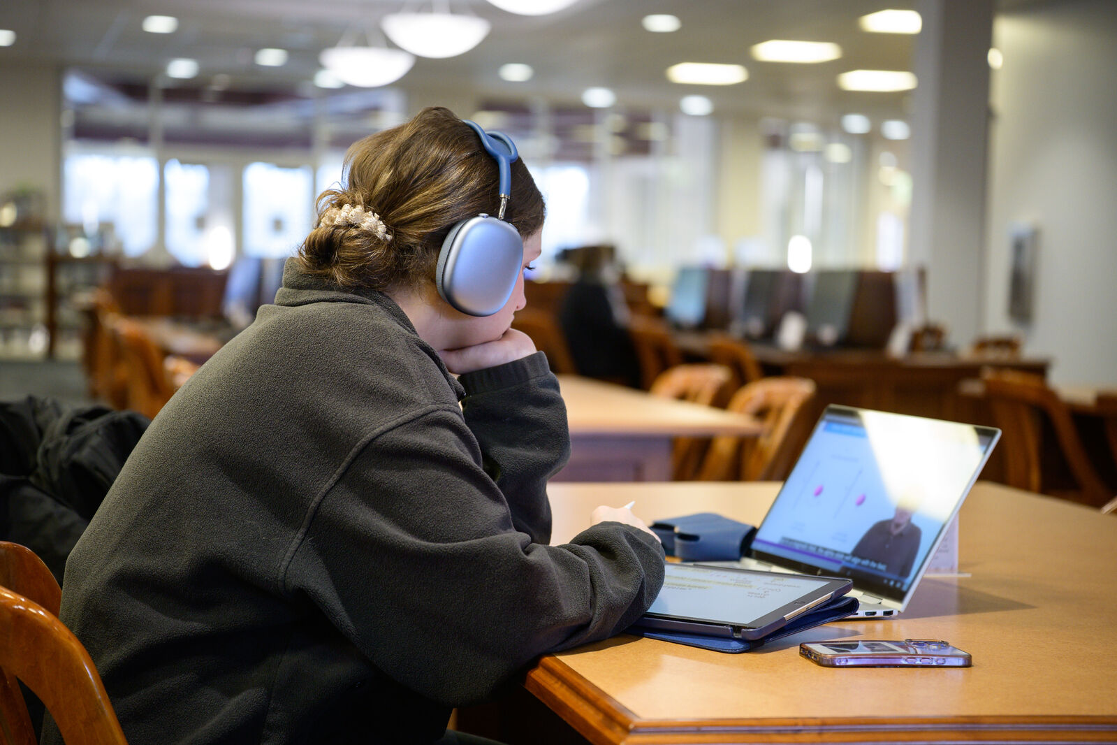 Person wearing headphones seated at library table looking at laptop.