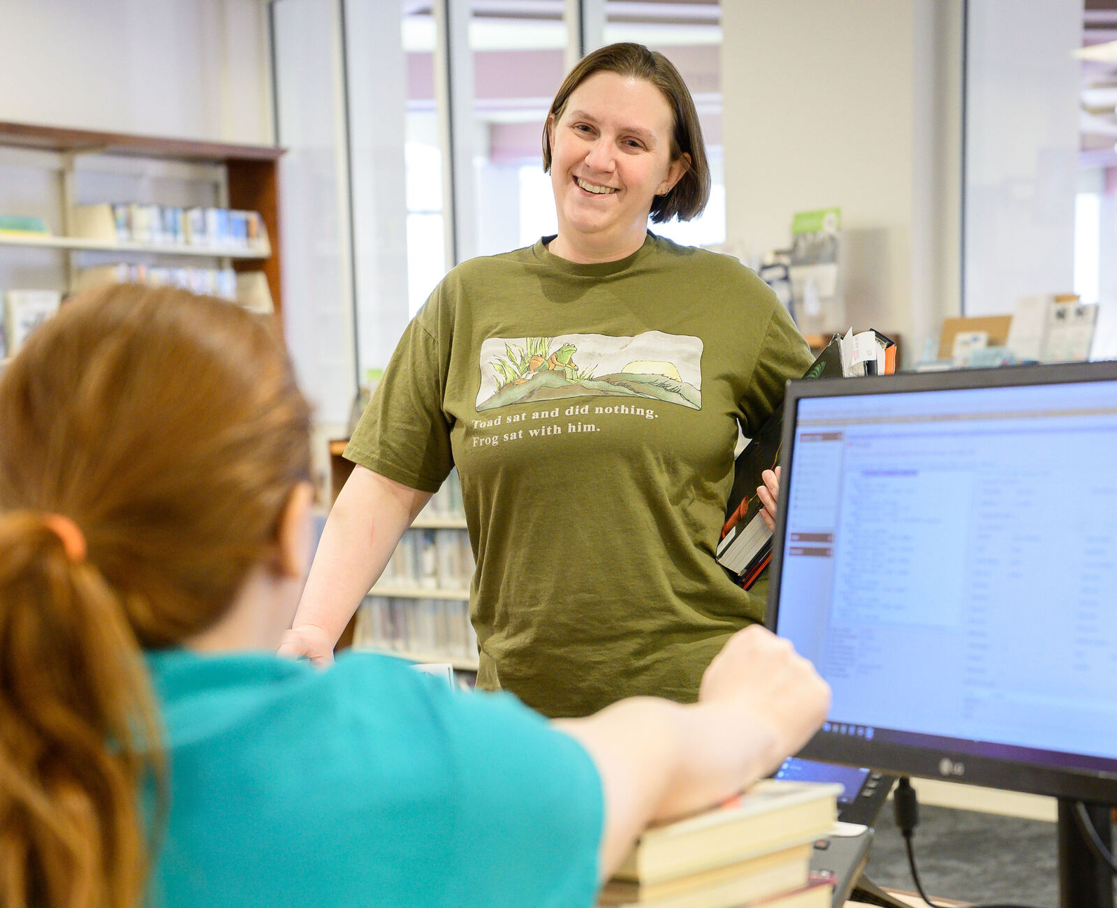 Individual smiling at a seated staff member while getting assistance at the reference desk.