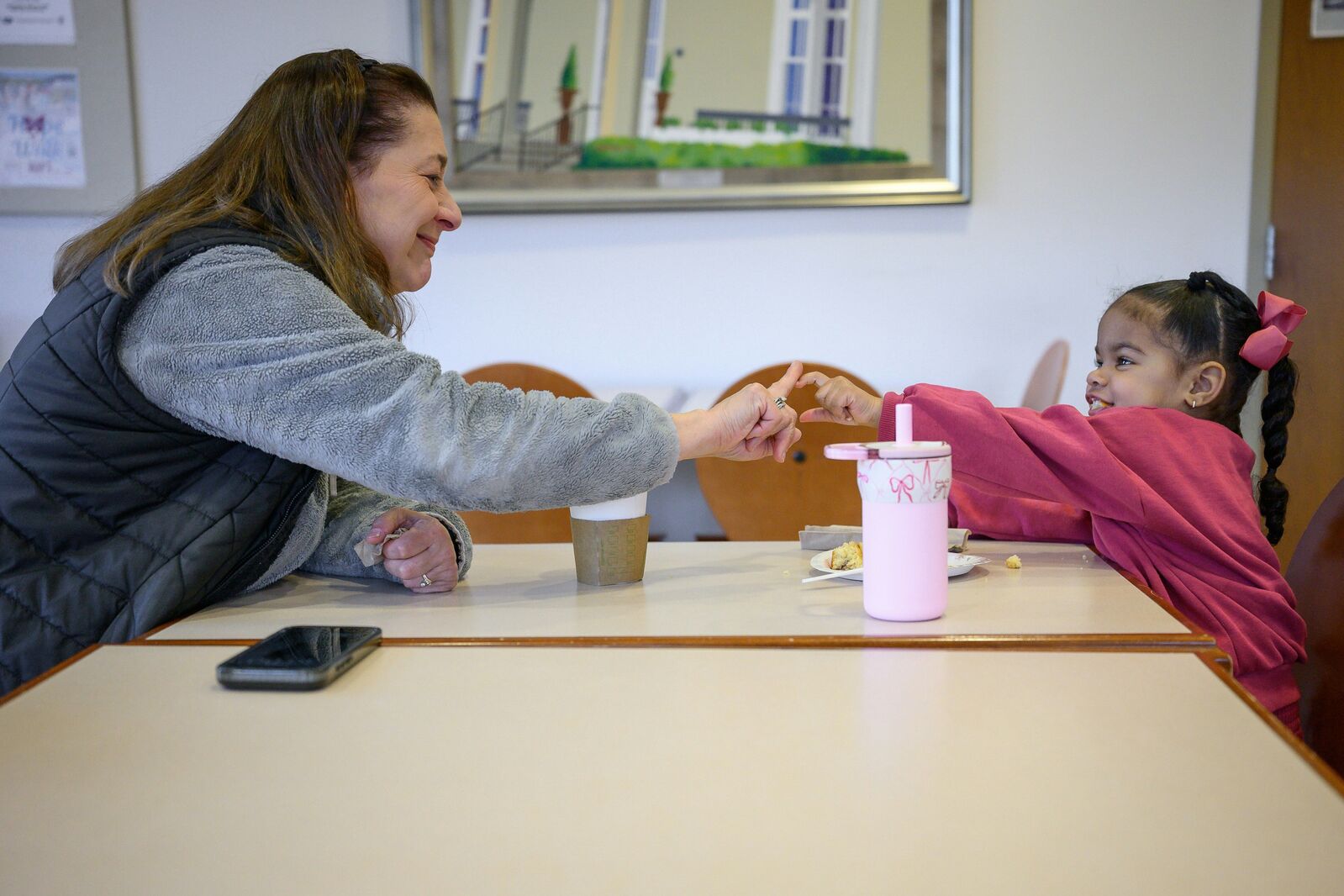 Adult and child seated across from each other at a table making a heart shape with their hands.