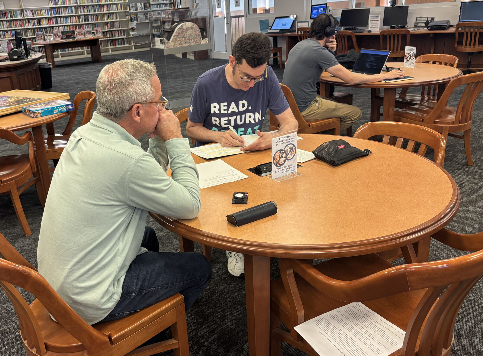Staff member writing in notary journal seated at a table with a patron.