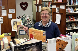 Individual holding up a book in the Friends bookstore smiling at the camera.