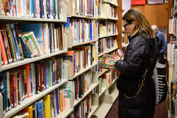 Individual holding a book while browsing a bookshelf in the Friends room.