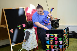 Librarian holding a ukulele and smiling at child at a felt board during storytime.