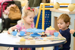 Two children seated at a table playing with a toy teaset