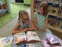 Two readers seated at a library table reading a book together.