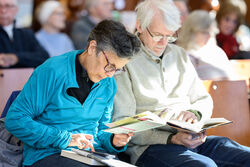 Two adults seated in library reading books.