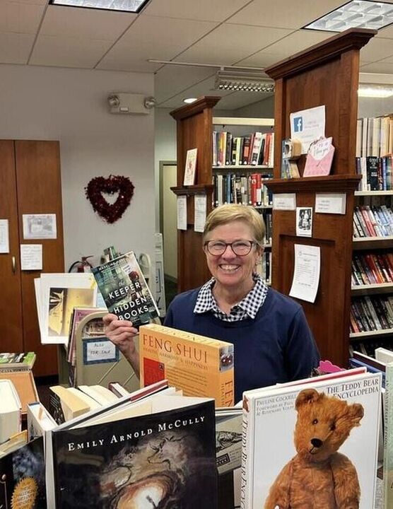 Individual holding up a book in the Friends bookstore smiling at the camera.