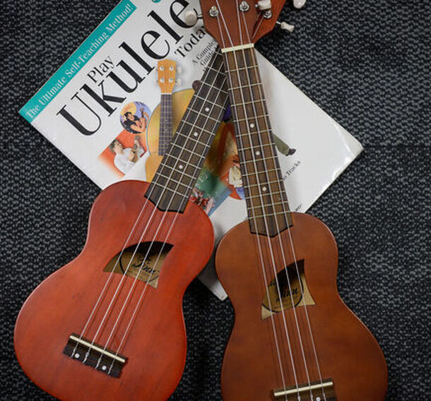 Two ukuleles resting on a carpet next to a copy of the book 'Play Ukulele Today'
