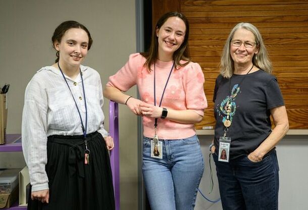 Three library staff members wearing lanyards smiling at the camera.
