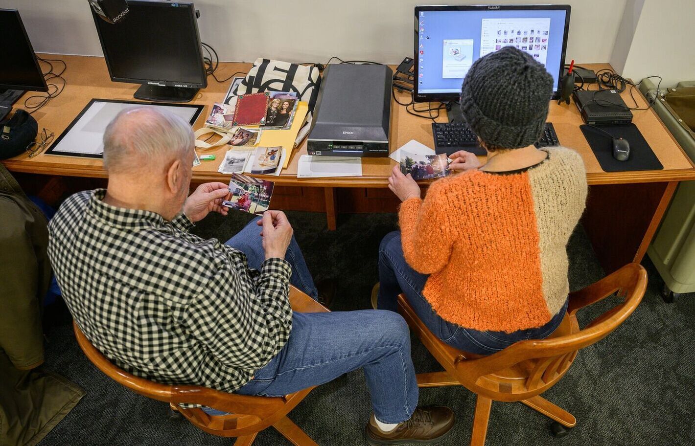 Two individuals seated browsing through photographs at a scanning station.