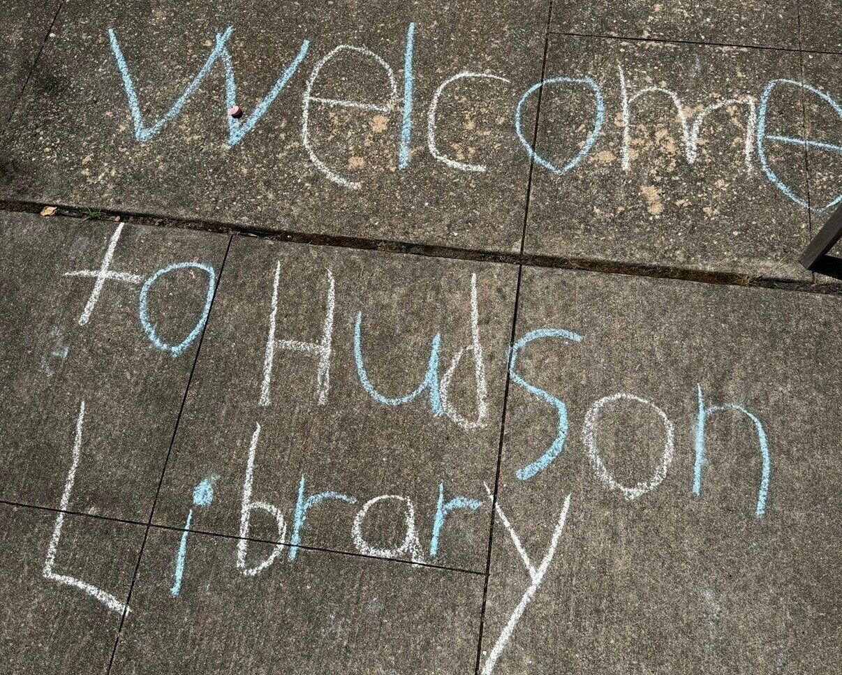"Welcome to Hudson Library" handwritten on sidewalk with chalk.