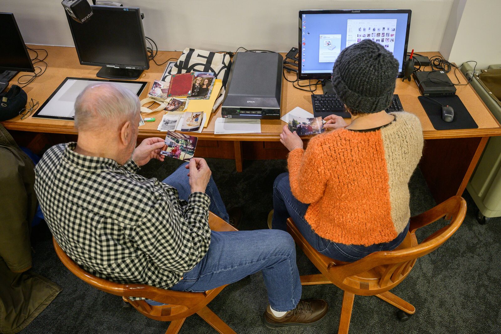 Two individuals seated browsing through photographs at a scanning station.